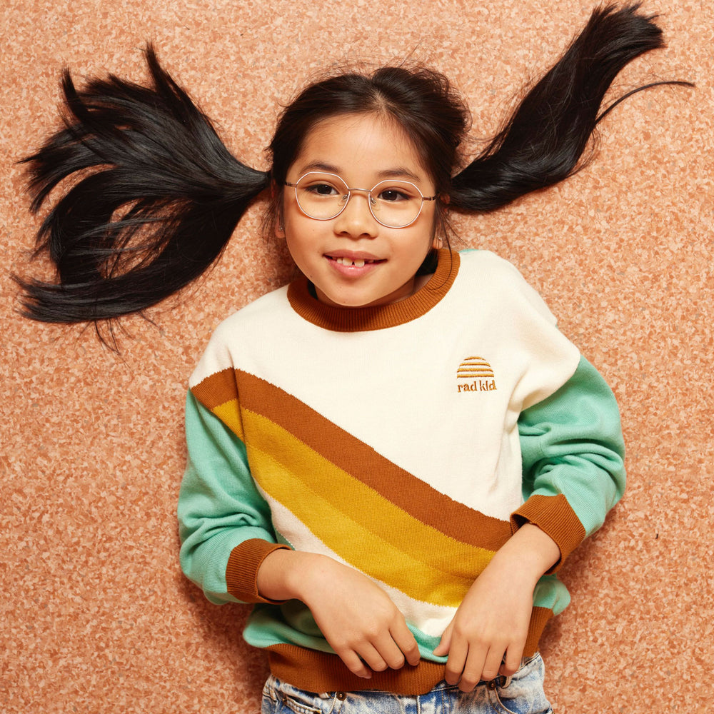 Child wearing a colorful sweater with a brand logo on a textured brown background